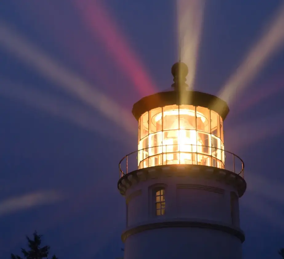Ein Leuchtturm bei Nacht, dessen helles Licht in den dunklen Himmel strahlt und durch die Beleuchtung der Umgebung Führung in unsicheren Zeiten symbolisiert.