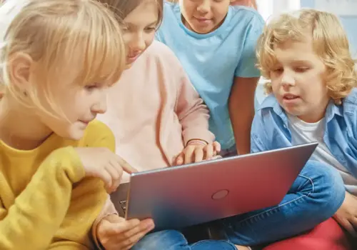 Vier kleine Kinder sitzen dicht beieinander, lächeln und schauen auf einen Laptop-Bildschirm. Sie denken darüber nach, wie frühe Neugier dazu beitragen kann, die Lernkultur in Unternehmen zu verbessern, indem sie Engagement und Teamarbeit fördert.