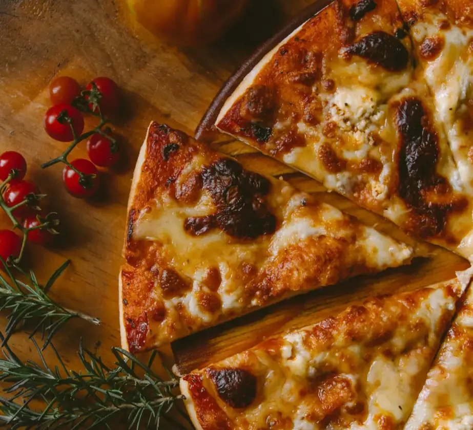 Eine in Scheiben geschnittene Käsepizza auf einer Holzoberfläche, garniert mit Rosmarinzweigen und einer Gruppe Kirschtomaten in der Nähe.