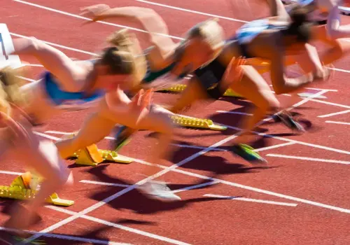 Mehrere Sportlerinnen werden in unscharfer Bewegung eingefangen, als sie aus den Startblöcken starten und dabei eine beeindruckende Geschwindigkeit und Konzentration an den Tag legen, die an Lernsprints erinnern, zu Beginn eines Sprintrennens auf einer Freiluftbahn.