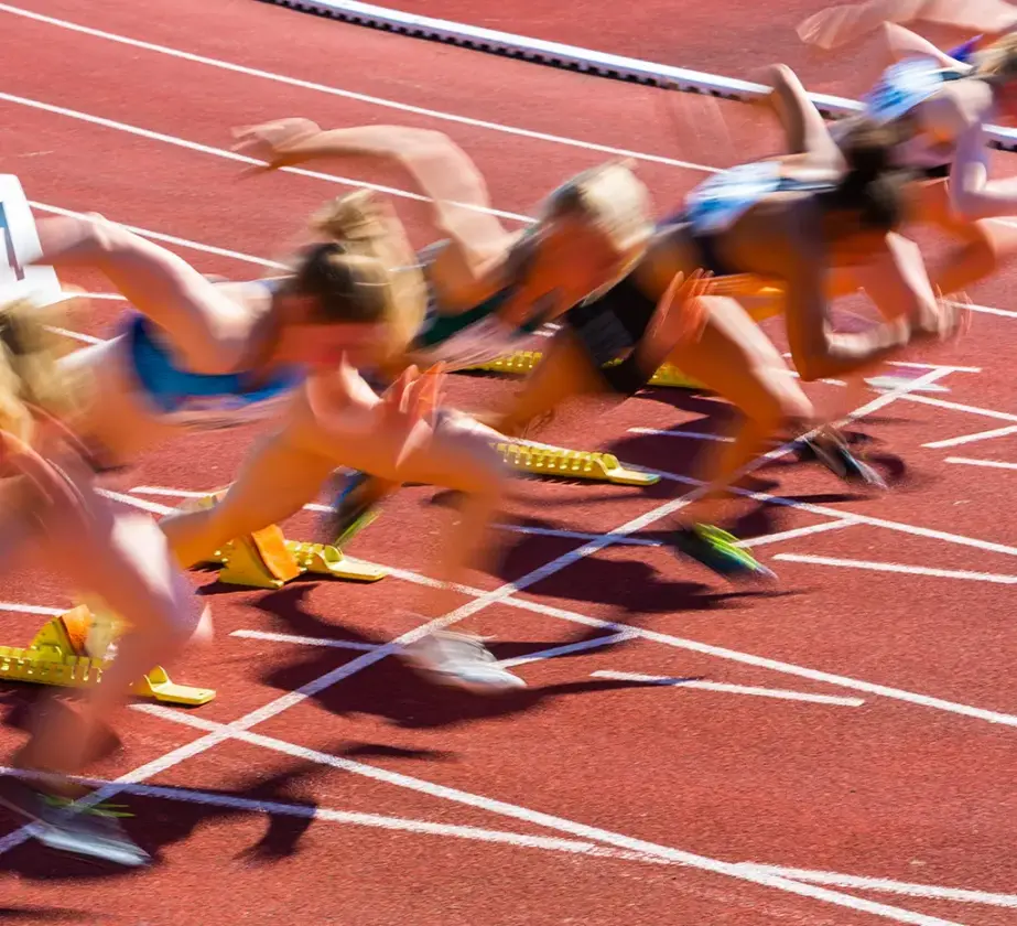 Mehrere Sportlerinnen werden in unscharfer Bewegung eingefangen, als sie aus den Startblöcken starten und dabei eine beeindruckende Geschwindigkeit und Konzentration an den Tag legen, die an Lernsprints erinnern, zu Beginn eines Sprintrennens auf einer Freiluftbahn.