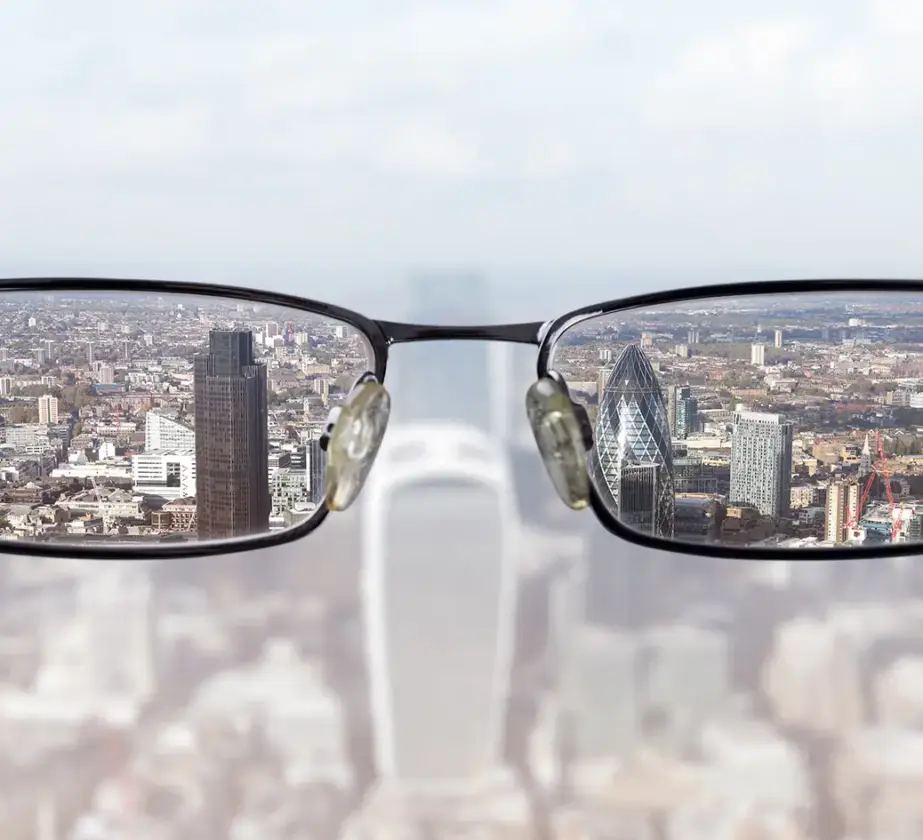 Eine verschwommene Stadtlandschaft wird durch die Brillengläser scharf abgebildet - so wie man Haltung durch Training verändern kann - und hebt hohe Gebäude und klare Details innerhalb der Brille hervor, während der Hintergrund unscharf bleibt.