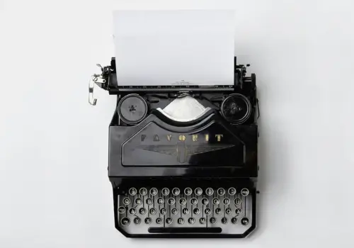 Eine alte schwarze Schreibmaschine mit einem leeren Blatt weißen Papiers, von oben gesehen vor einem schlichten weißen Hintergrund - eine Mischung aus zeitlosem Design und der Verheißung zukünftiger Fähigkeiten, die geschrieben werden können.