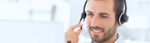 Ein lächelnder Mann mit Kopfhörern sitzt an einem Computer und scheint zu sprechen oder zuzuhören – in einer hellen, modernen Büroumgebung, die die ansprechende Atmosphäre erfolgreicher Trainings- und Coachingprojekte perfekt einfängt.