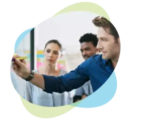 Ein Mann schreibt mit einem gelben Marker auf ein Whiteboard, während zwei Kollegen in einer modernen Büroumgebung, umgeben von pastellgrünen und -blauen abstrakten Formen, aufmerksam zusehen – so entsteht eine inspirierende Atmosphäre, die sich ideal für Weiterbildungen in den Bereichen Führung und Kommunikation eignet.