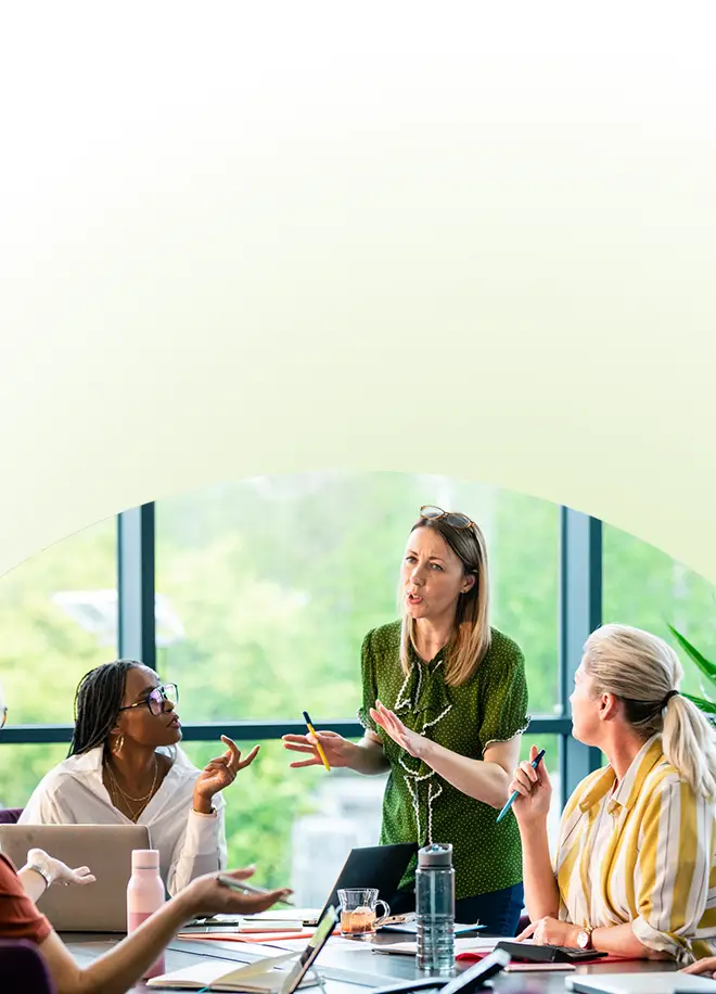Drei Frauen an einem Konferenztisch, die an einer Diskussion im Rahmen eines Führungstrainings für Führungskräfte teilnehmen.