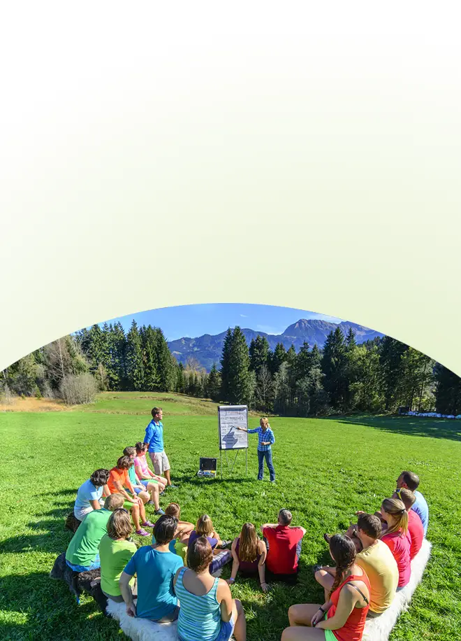 Eine Gruppe von Fachleuten sitzt im Kreis auf einer Wiese und beobachtet, wie eine Frau mithilfe eines Whiteboards eine Rhetorik-Schulung leitet.