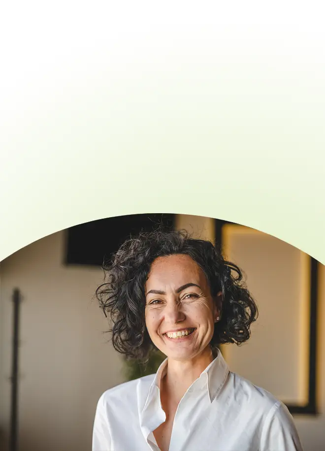 Eine lächelnde Frau mit dunklem, lockigem Haar, die ein weißes Hemd mit Kragen trägt, bei einem Seminar zur Persönlichkeitsentwicklung.