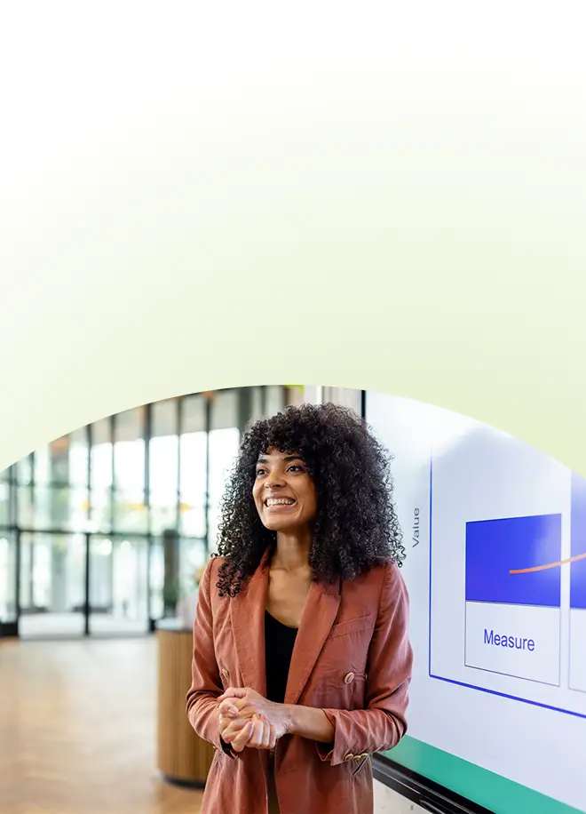 Eine lächelnde Frau in einem rostfarbenen Blazer steht vor einer digitalen Anzeige, die für das Präsentationstraining für Fach- und Führungskräfte verwendet wird und ein Diagramm mit der Überschrift Value and Measure zeigt.