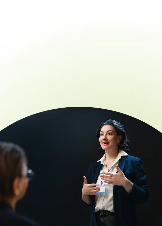 Eine Frau in einem Blazer und mit Namensschild gestikuliert, während sie im Rahmen eines Rhetoriktrainings für Fach- und Führungskräfte mit jemandem außerhalb des Bildausschnitts spricht.