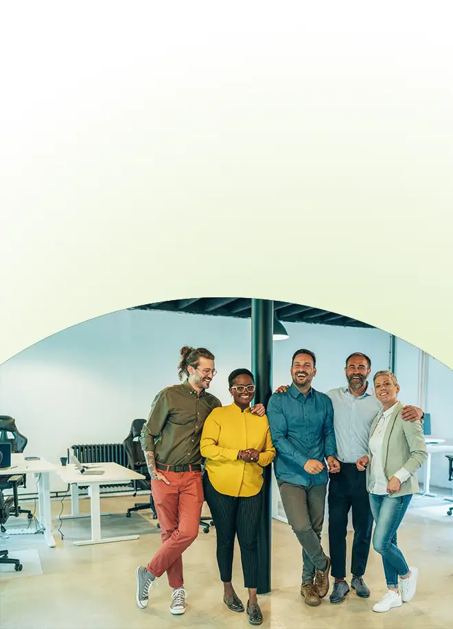Fünf Kollegen unterschiedlicher Herkunft, die während einer Veranstaltung zum Thema Teamentwicklung für Unternehmen gemeinsam in einem Büro lächeln.
